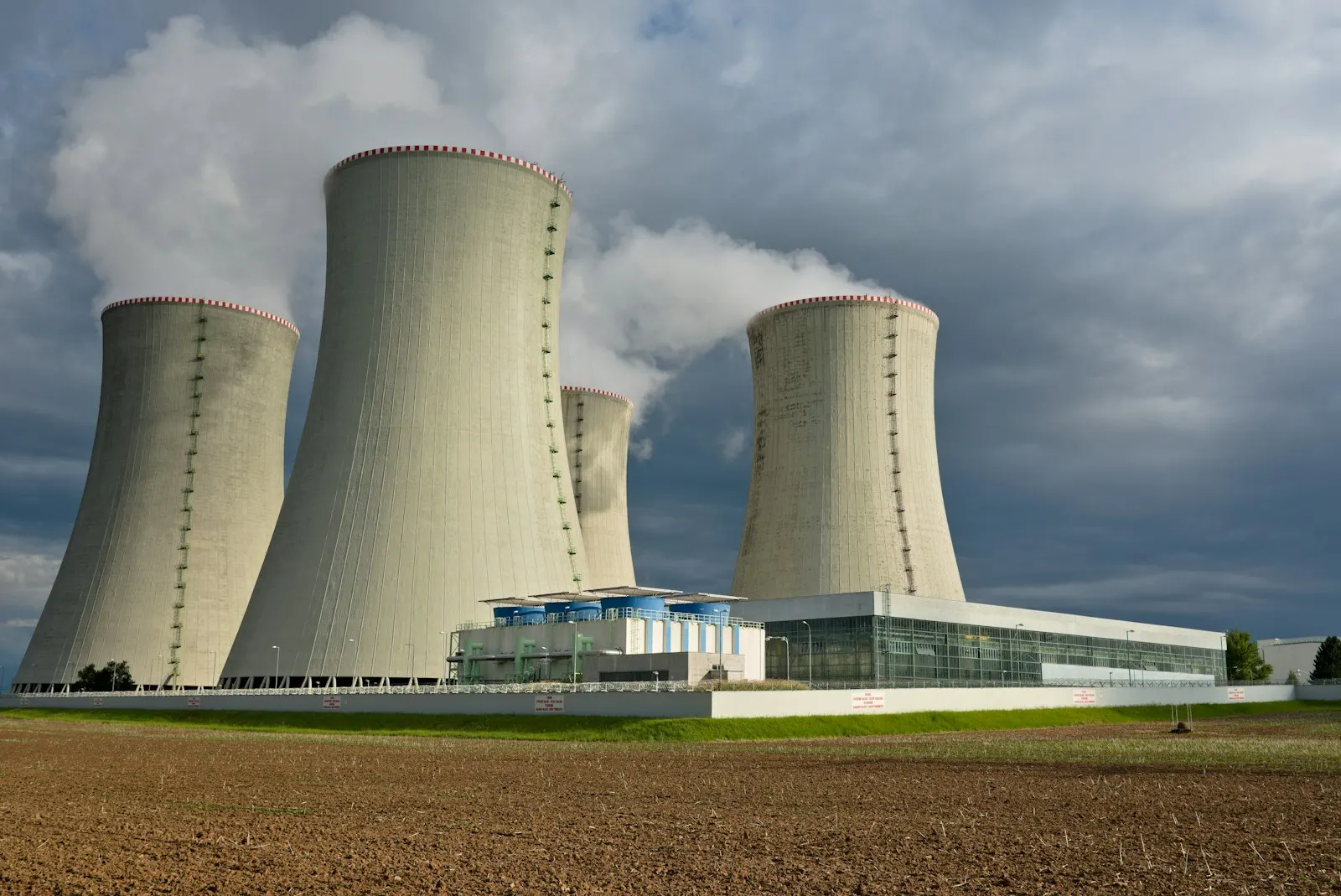 Four large concrete cooling towers emitting steam under a dark cloudy sky — illustrative image