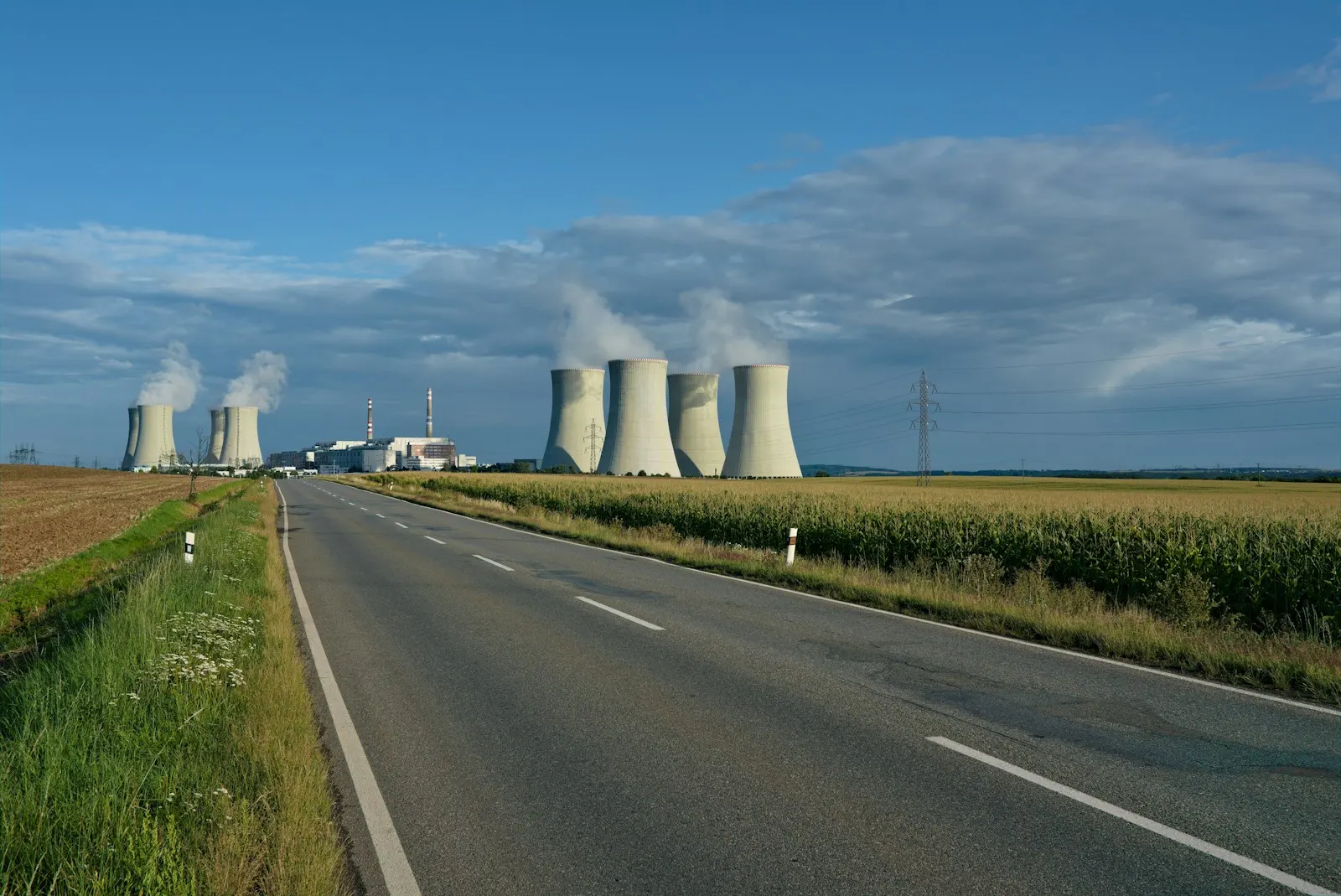 gray asphalt road between green grass field under blue sky during daytime — illustrative image